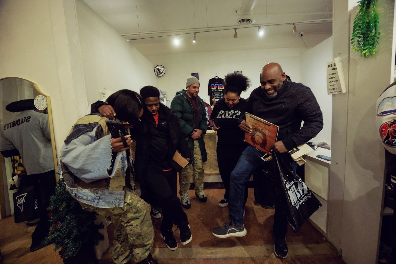 Guests laughing and dancing by the shop counter, one holding a vinyl record and a shopping bag